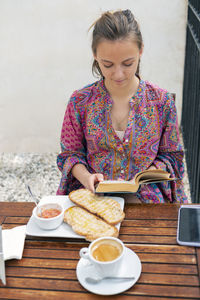 Woman having toast for breakfast on a bar terrace and reading a book person