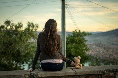 Rear view of woman sitting on retaining wall at sunset