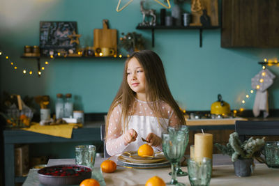 Child girl is sitting at a festive table set for christmas and smiling