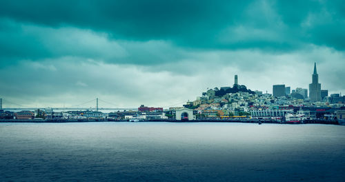 View of buildings by sea against cloudy sky