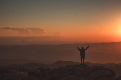 Man standing on rock against sky during sunset