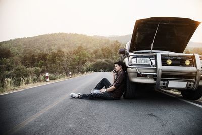 Man sitting by car on road