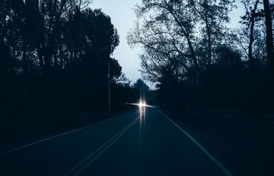 Empty road along trees at dusk