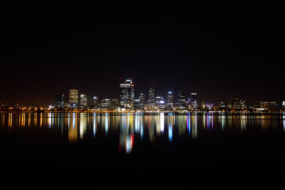 Illuminated cityscape by sea against clear sky at night