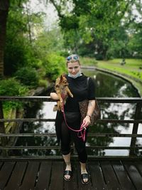 Portrait of young woman carrying puppy while standing on footbridge in park