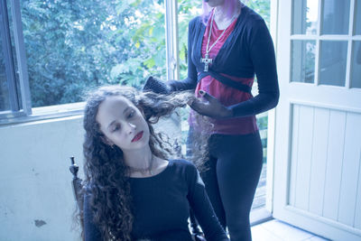 Midsection of hairdresser combing woman hair at home