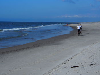 People riding bicycle on beach against sky