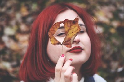 Close-up portrait of woman looking through dry leaf