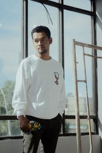Portrait of young man standing against window in building