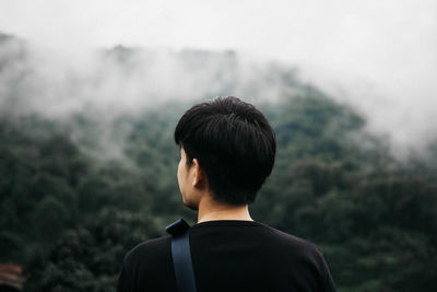 Rear view of man looking at mountain during foggy weather