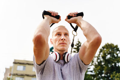 Low angle portrait of man holding camera against sky