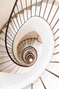 From above of white spiral stairs with wooden banister in bright contemporary building