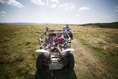 Friends riding off-road vehicle and quadbike on grassy field against sky