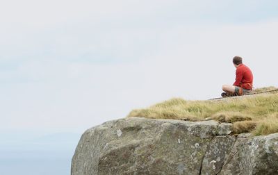 Side view of man sitting on rock against sky