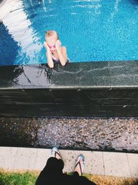 Low section of woman standing by girl in swimming pool