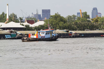 Boats in river by buildings in city against sky