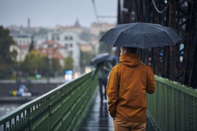 Rear view of man standing by railing in city during rainy season