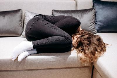 Teenager girl closing her face with hands and crying on couch. puberty and depression