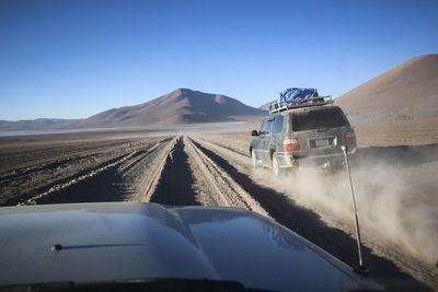 Off-road vehicles moving on dirt road against clear blue sky during sunny day
