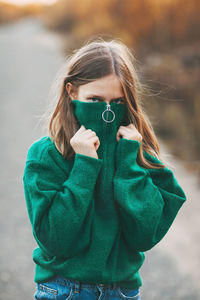 Beautiful teenage girl with blonde hair and blue eyes in a warm green sweater in an autumn park.
