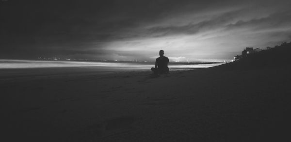 Man sitting on beach against sky