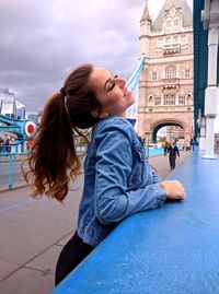 Smiling woman with eyes closed standing on tower bridge in city
