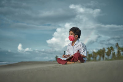 Girl looking at camera while sitting on land against sky