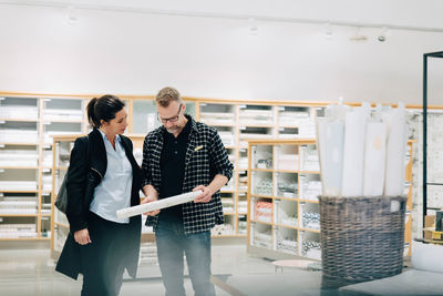 Salesman showing wallpaper to female customer in store