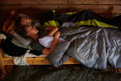 High angle view of couple with blankets sleeping on bed in log cabin