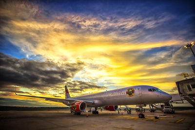 Airplane on runway against sky during sunset