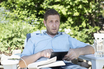 Mid adult man looking away while using digital tablet on lounge chair at yard