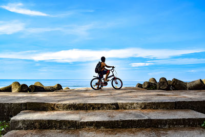 Boy riding bicycle on rocks against sky