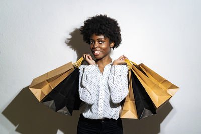 Smiling young woman carrying shopping bags while standing against white background