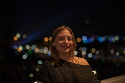 Portrait of smiling young woman in city at night