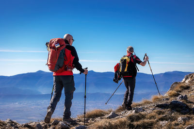 Rear view of two men standing on mountain against clear blue sky