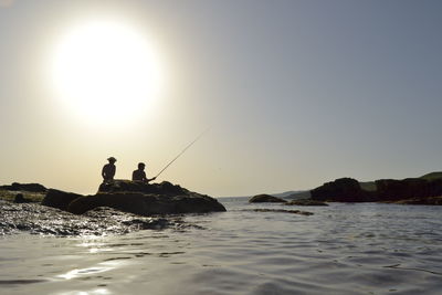 Silhouette people fishing in sea against clear sky during sunset