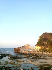 Cliff by sea against clear blue sky