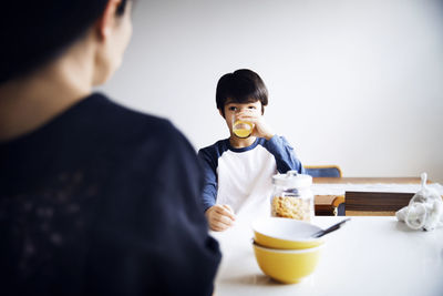 Boy drinking juice while eating breakfast with mother at home