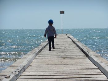 Rear view of man standing on pier at sea against clear sky