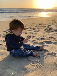 Boy on beach against sky during sunset