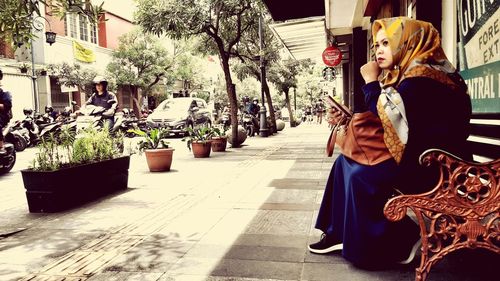 Side view of woman sitting on footpath