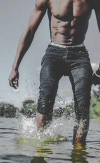 Midsection of man wading in lake against sky