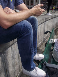 Low section of man holding camera while sitting outdoors