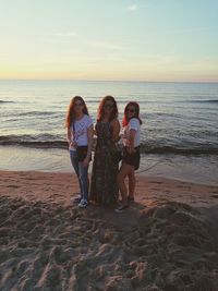 Portrait of female friends standing at beach during sunset