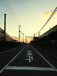 Road by railroad tracks against sky during sunset