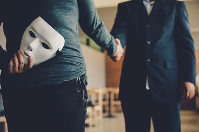 Businesswoman hiding mask while shaking hands with colleague in office