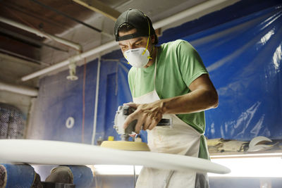 Worker using sander machine on surfboard in workshop