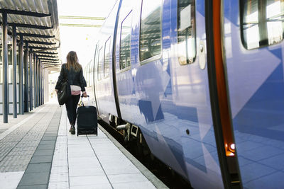 Rear view of businesswoman pulling wheeled luggage on railroad station platform