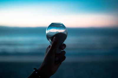 Close-up of hand holding sea against sky during sunset