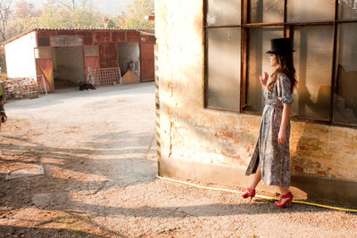 Young woman standing on footpath by window of old building